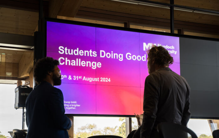 University students standing in front of a screen which says 'Students Doing Good Challenge'