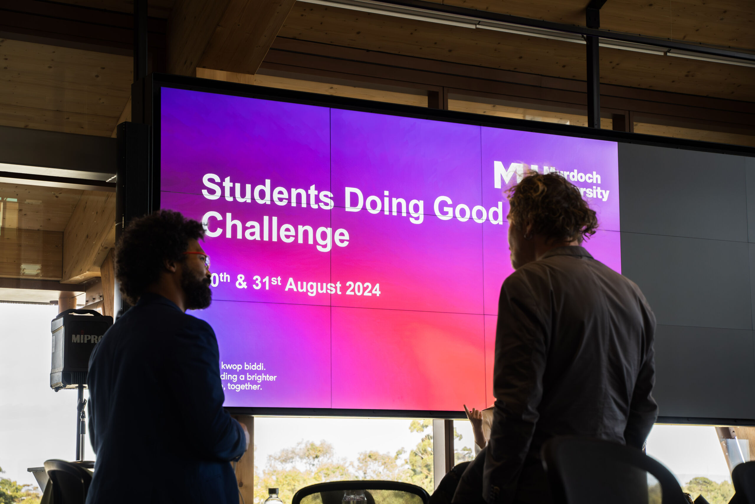 University students standing in front of a screen which says 'Students Doing Good Challenge'